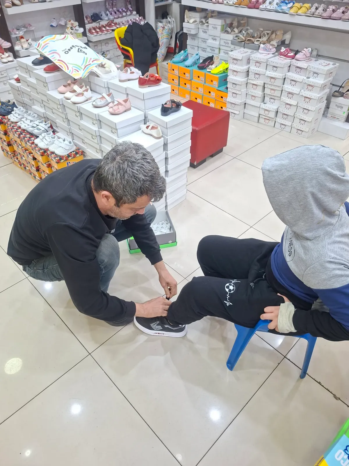Mağazada bir çocuğun ayakkabısının bağcığı bağlanırken